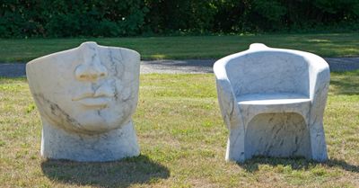 deux sculptures en pierre représentant un homme et une chaise dans l'herbe