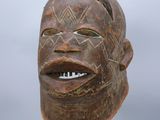 une image représentant un masque en bois posé sur un socle, sur fond gris