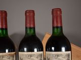 three bottles of red wine sit on a wooden table