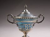 an ornate silver and blue vase with handles on a white surface