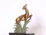 une statue en bronze représentant un cerf posé sur une plante verte