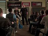 several people sitting in chairs in a room with a man standing in front of them