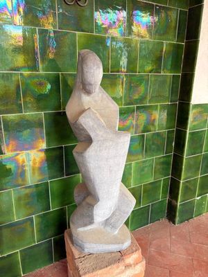 a statue of a woman sitting on a block in front of a green tiled wall