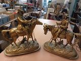 two bronze statues of men riding horses on a table