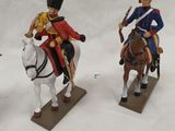 three figurines of soldiers riding on horses on a white surface