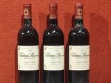 Trois bouteilles de vin sont posées sur une table, avec un mur rouge en arrière-plan.