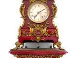 une horloge rouge et dorée posée sur une étagère, sur fond blanc