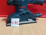 un gros plan d'une ponceuse posée sur une table, avec une boîte rouge en arrière-plan