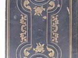 an old black book with gold designs on it sitting on a white surface