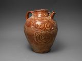 un vieux vase marron orné de motifs en spirale sur un fond gris