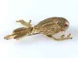 une image représentant une broche en forme d'oiseau doré posée sur une surface blanche