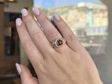 woman ' s hand holding a red and white diamond ring in front of a window