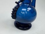 a blue vase with a black handle on a white table