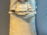 une poupée allongée dans un lit, recouverte d'une couverture