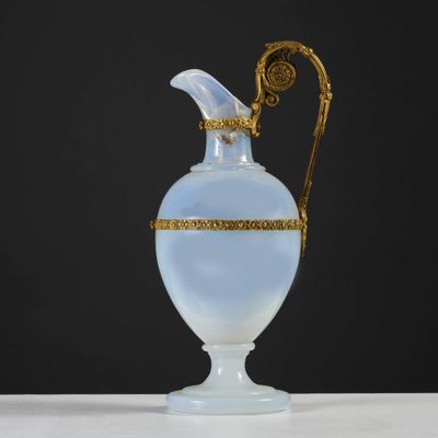 an antique glass vase with gold trim and handle on a white table