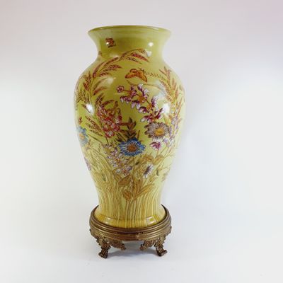 a yellow vase with flowers on it sitting on a stand