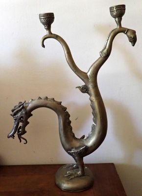 une sculpture en métal représentant un dragon, posée sur une table avec deux bougies