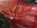 une voiture rouge cabossée, garée sur le bord de la rue
