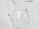 un pichet en verre transparent posé sur une surface blanche, avec un fond blanc
