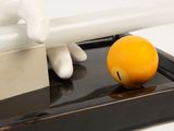 a white glove holding a knife next to an orange ball