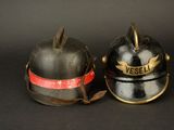 pair of antique fire helmets on a black background with a red ribbon