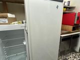 a small white refrigerator in a room with a shelf