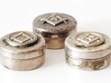 three silver containers with initials on them sitting on a white surface