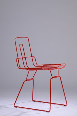 une chaise en métal rouge posée sur un sol blanc
