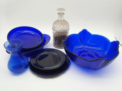 un bol en verre bleu, une assiette bleue et un bol noir posés sur une surface blanche