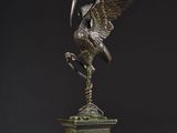 bronze statue of a bird on a pedestal with a clock in the background
