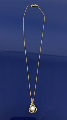 un collier en or orné d'un pendentif en perle sur un fond bleu