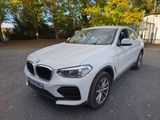 un SUV BMW blanc garé sur un parking, avec des arbres en arrière-plan