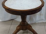 marble topped table with wooden pedestal on tiled floor in front of a white curtain