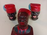 trois figurines représentant des hommes noirs coiffés de chapeaux rouges