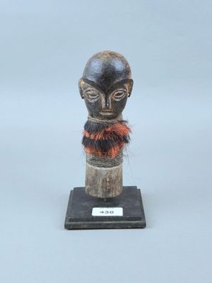 statue représentant la tête d'un homme, posée sur un socle en bois, avec un foulard rouge autour du cou