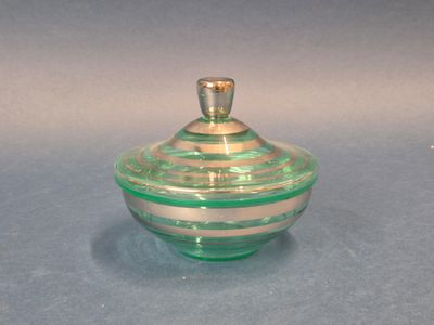 un bocal en verre vert avec un couvercle doré, posé sur un fond bleu