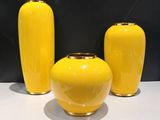 trois vases jaunes posés sur une table blanche, sur fond noir