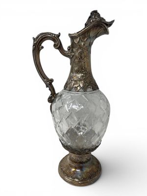 an antique silver and glass pitcher on a stand on a white background