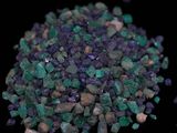 purple and green crystals are scattered on a black surface