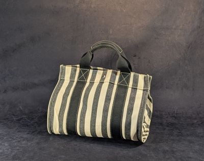 un sac à main rayé beige et noir posé contre un mur gris