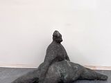 statue représentant une femme assise sur le dos d'un homme, posée sur un plancher en bois