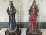 two figurines that are under a glass dome on a table