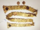 three gold bracelets and a coin on a white surface