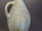 un grand vase vert muni d'une anse, sur fond gris