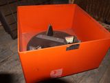 une boîte orange contenant un disque, posée sur un plancher en bois