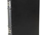 an old book with a black cover sitting on top of a white table