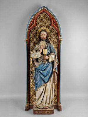une statue de Jésus tenant une coupe devant un mur