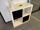 a white shelf with two black bins and a roll of toilet paper on it