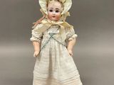 une poupée ancienne en porcelaine représentant une jeune fille vêtue d'une robe et d'un bonnet