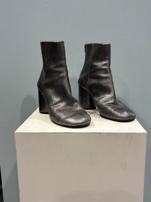 black leather ankle boots on a white pedestal in front of a blue wall